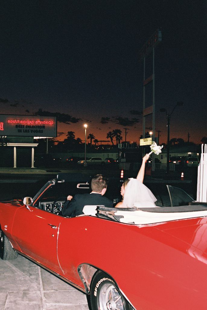 bride and groom celebrating in red convertible